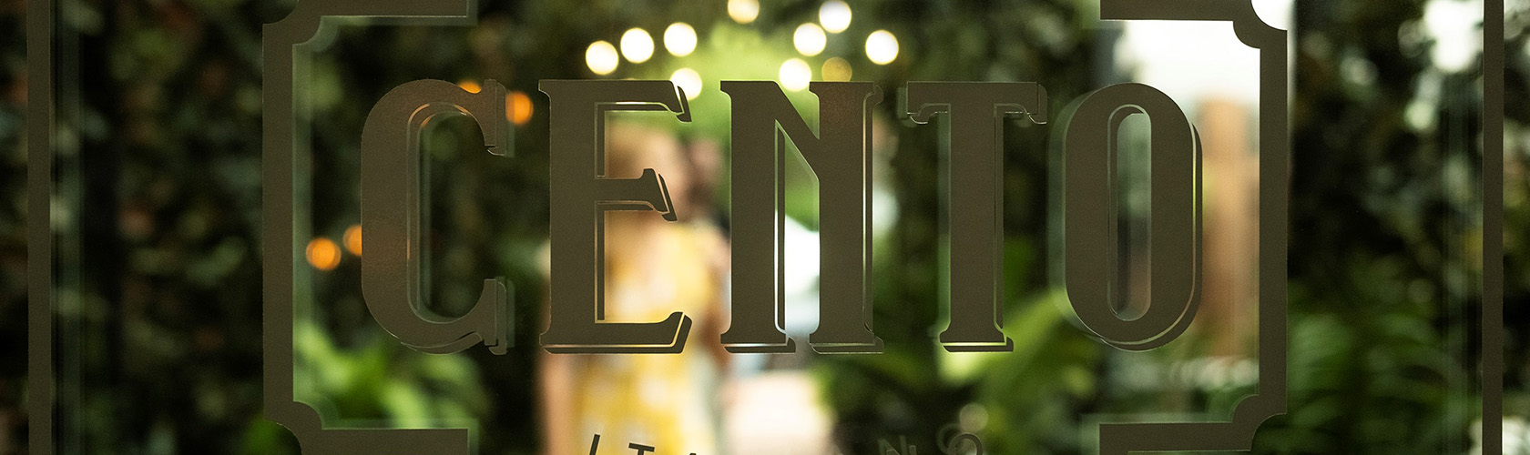 Cento restaurant logo on glass with greenery in background